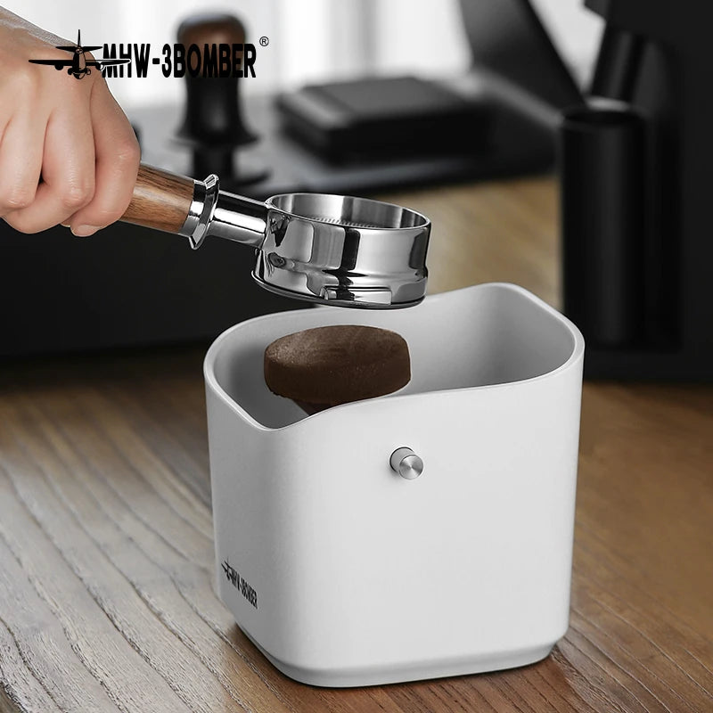 Hand using a coffee tamping tool to press coffee grounds into a white container on a wooden surface.