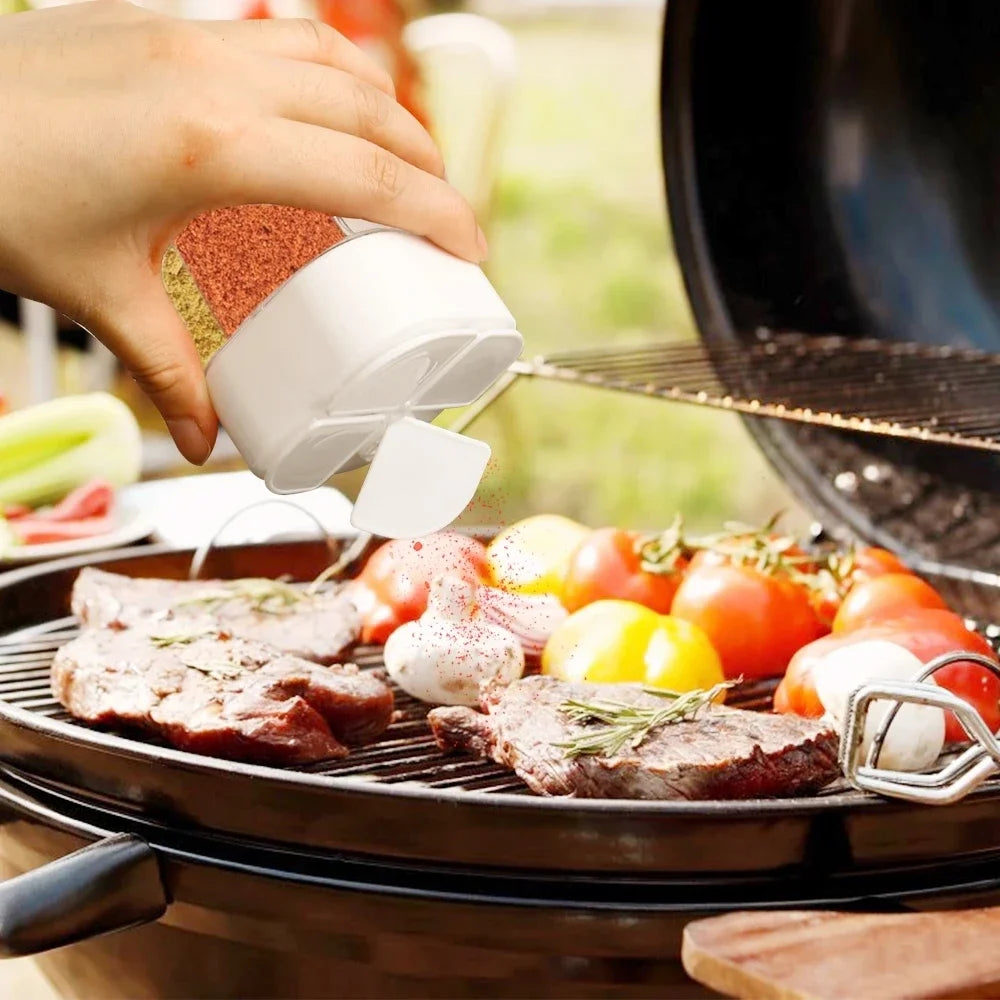 Person seasoning meat and vegetables on a grill with a shaker.