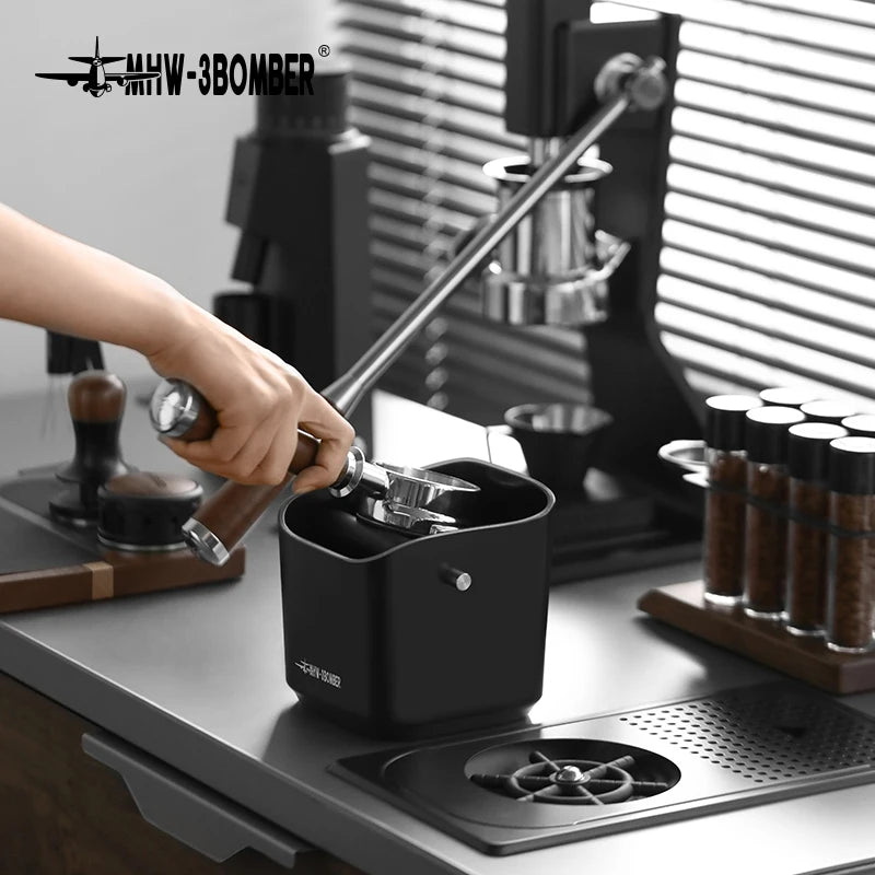 Person using a manual coffee grinder on a kitchen counter with coffee beans and equipment in the background.