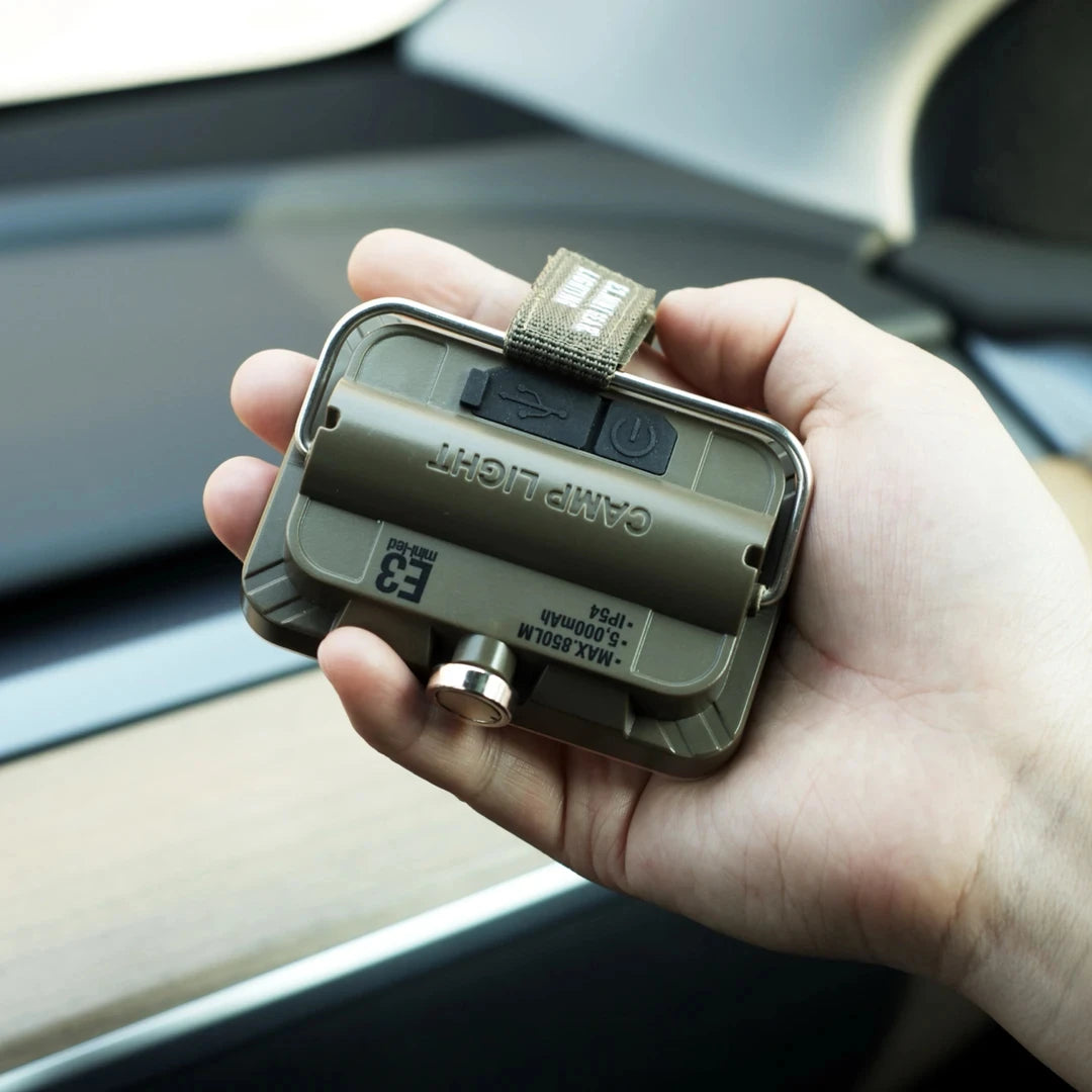 Hand holding a camping light device inside a vehicle.