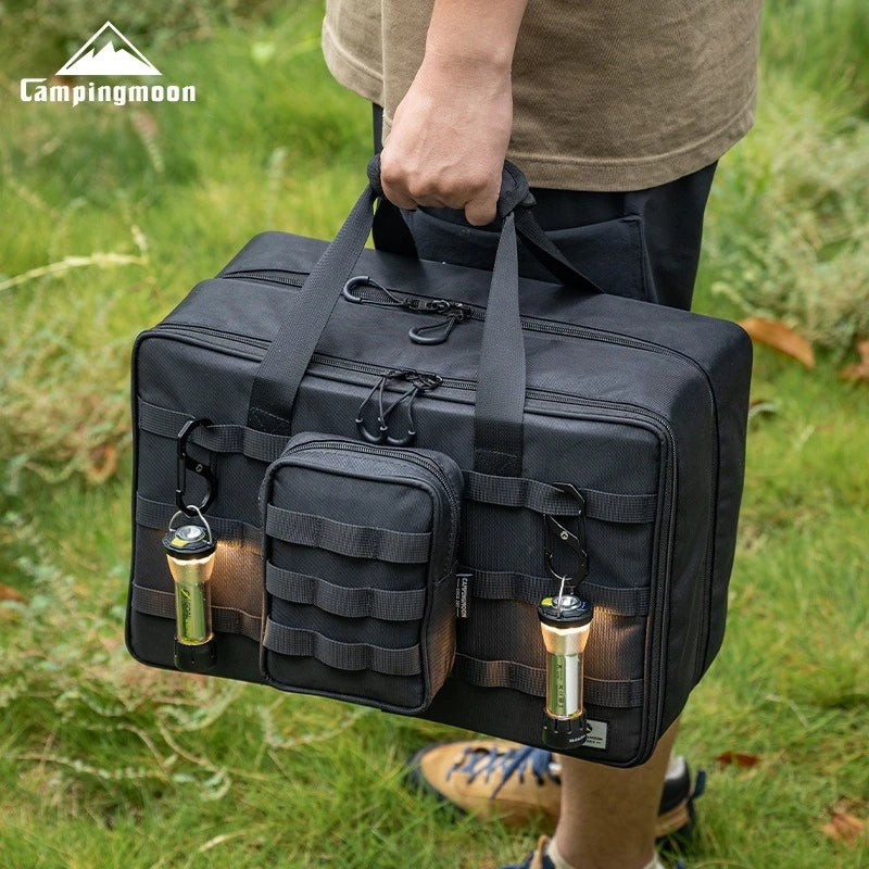 Person holding a black tactical bag with campingmoon logo in the background