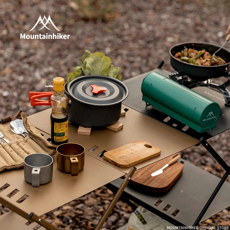 Camping setup with cookware, stove, and utensils on a table outdoors.