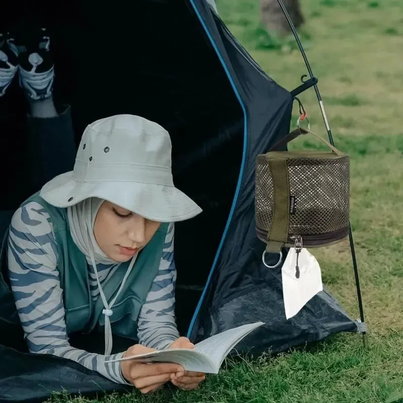 Person reading a book while sitting inside a tent outdoors