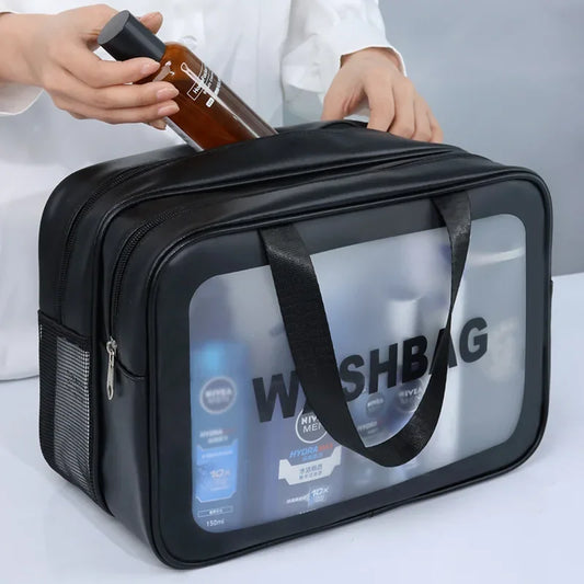 Black travel wash bag with clear front panel displaying grooming products, held by a person.